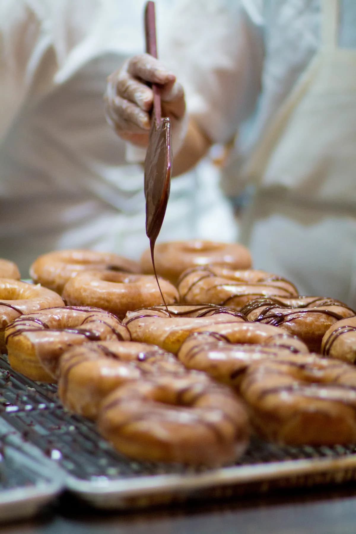 A baker glazing freshly made Johnny Doughnuts.
